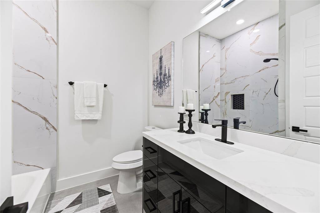 This elegant bathroom mixes sleek and luxurious details. A black vanity with a crisp white countertop pairs perfectly with modern black fixtures and a large mirror. Marble-like tiles on the walls bring a touch of class, while stylish decor and a roomy shower complete the look.