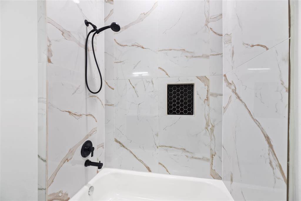 This bathroom features a modern shower with elegant white marble-patterned tiles and black fixtures, offering a sleek, contemporary look.