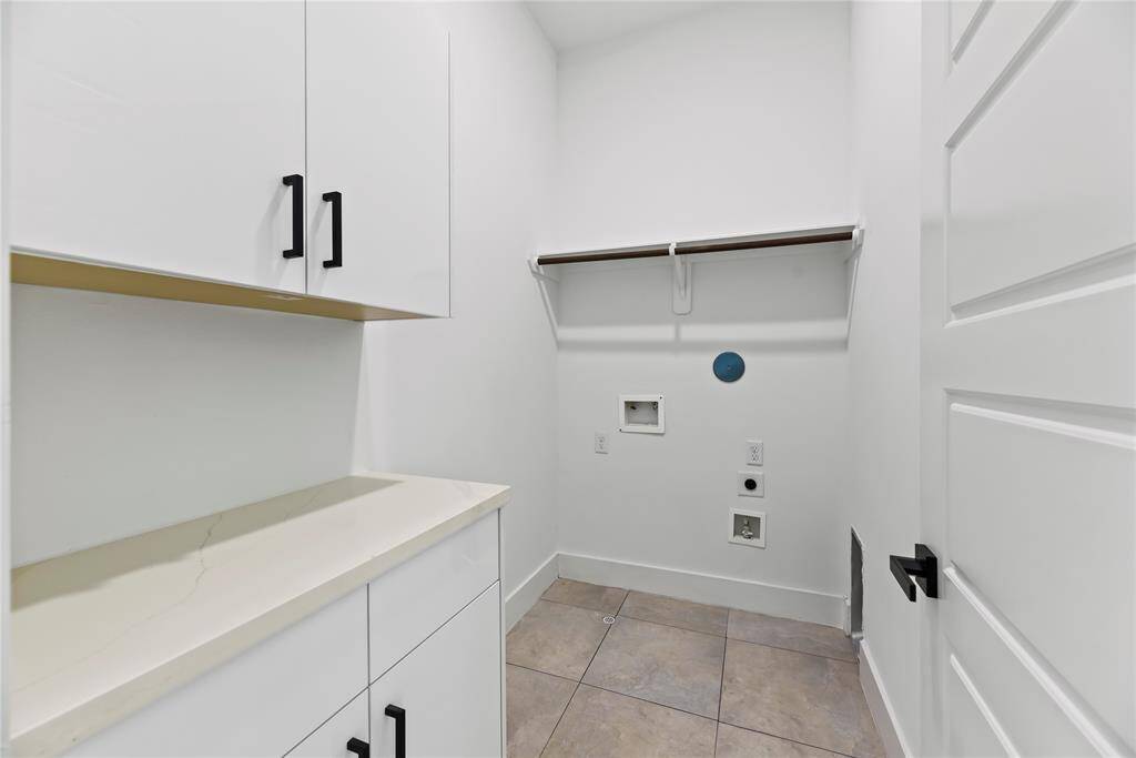 This modern laundry room keeps things clean and simple with white cabinets and plenty of countertop space. There’s room for both a washer and dryer, tiled floors for easy cleanup, and a handy hanging rod that makes laundry day a little easier.