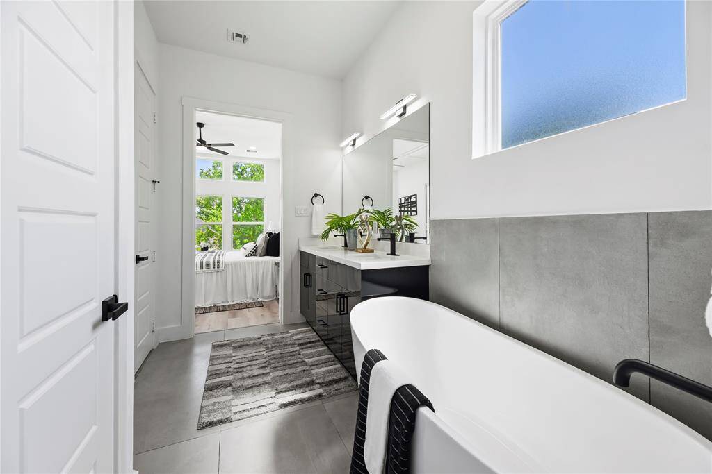 This modern bathroom features a sleek design with a freestanding bathtub, large mirror, and stylish vanity. Natural light pours in through a frosted window, complementing the neutral tones and contemporary fixtures.