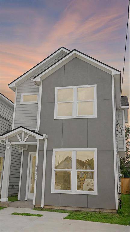 This modern, two-story home features a sleek gray exterior with white trim and large windows, providing a bright and inviting appearance. The entrance is covered, and there is a small lawn area alongside a spacious driveway.