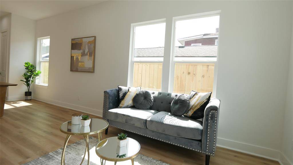 Bright and airy living space with large windows, light wood flooring, and modern decor. Features a stylish gray sofa, accent tables, and artwork, creating a cozy and inviting atmosphere.