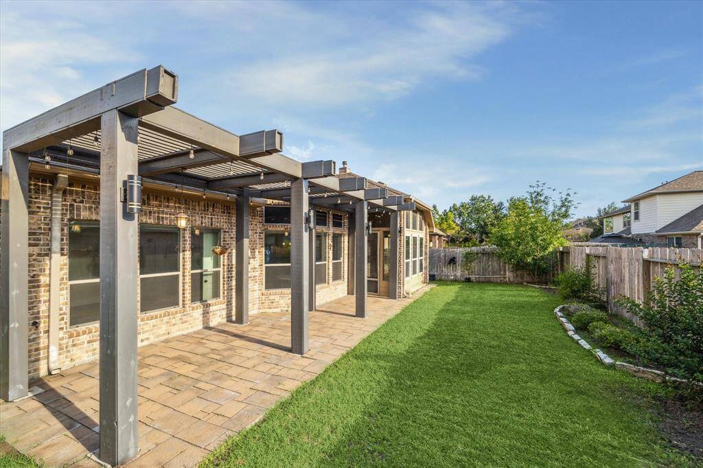 Step into your outdoor retreat—featuring a sunroom, a modern pergola over an extended paved patio, and a beautifully maintained lawn with lush green grass and neatly trimmed bushes. Perfect for relaxing or entertaining year-round.