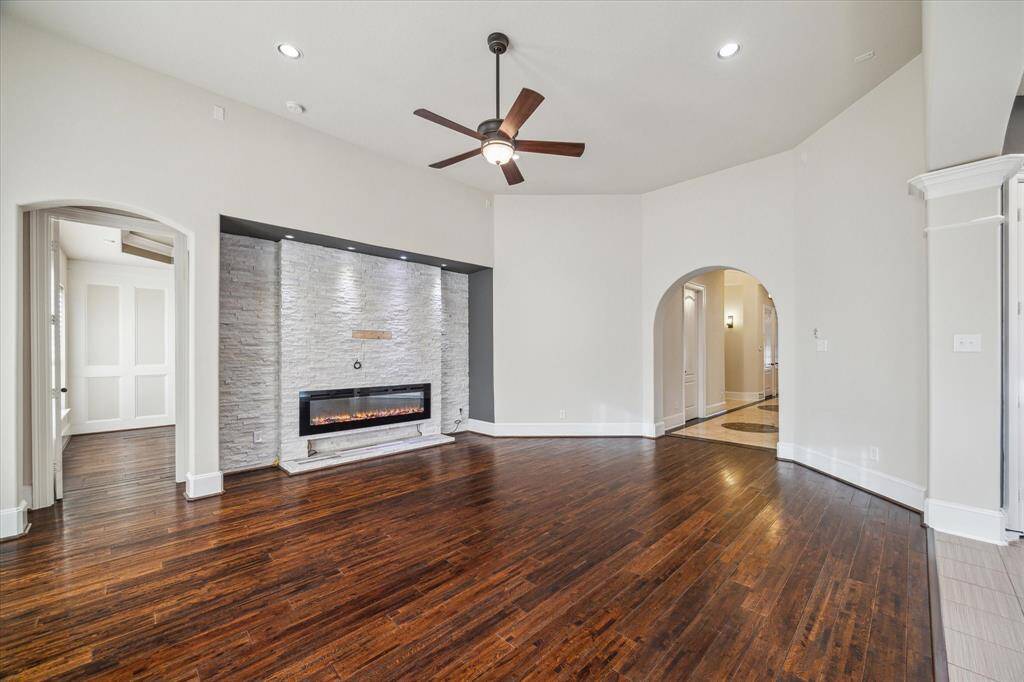 Soaring ceilings and rich engineered wood flooring create an airy, inviting living space—anchored by a sleek mock fireplace set against a bold brick accent wall for a touch of modern warmth.