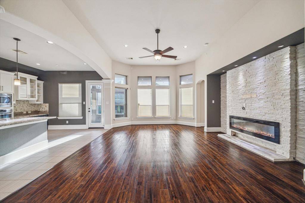 Another view of the open-concept living and kitchen area reveals oversized windows along the back of the home, filling the space with natural light and offering a glimpse into the cozy sunroom retreat.