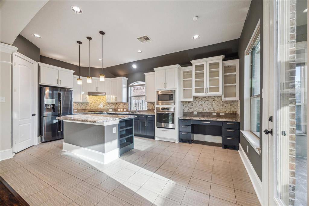 This thoughtfully designed kitchen features dual-tone cabinetry, a central island ideal for prepping or casual meals, and abundant storage thanks to extensive cabinetry. A built-in desk adds a functional touch—perfect for homework, planning, or working from home.