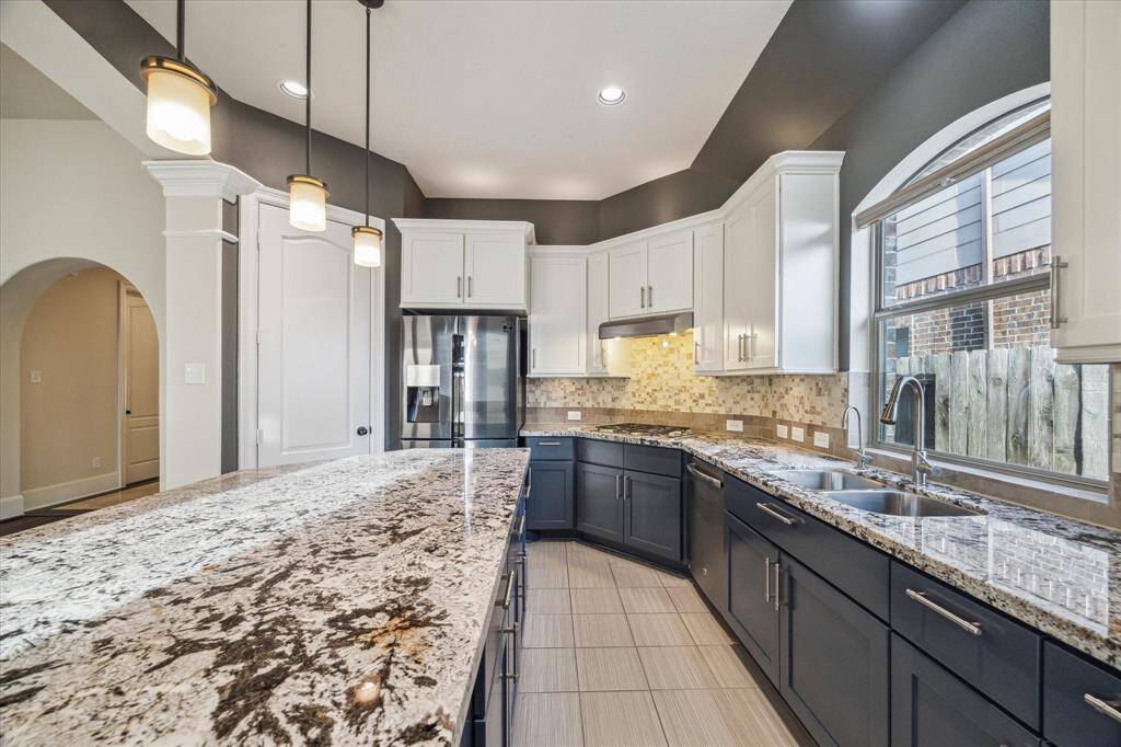 A closer look at the kitchen reveals granite countertops, a sleek gas cooktop, and modern stainless steel appliances—including the refrigerator—all designed to blend style and everyday functionality.