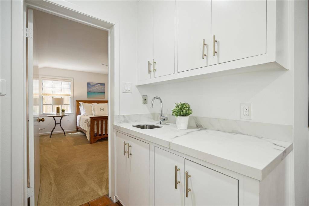 Porcelain countertops, a stainless-steel sink, and ample cabinetry define this elegant guest house wet bar. Ideal for entertaining with sophistication. Every detail complements the home’s elevated style.