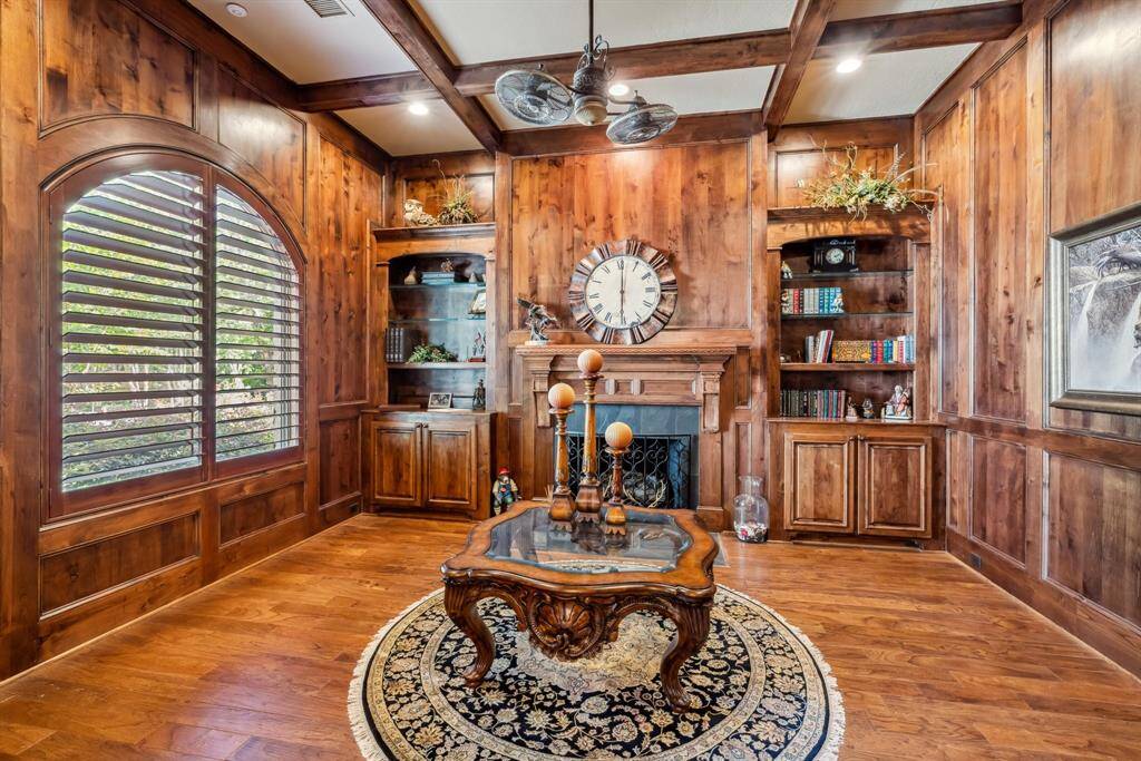 This photo features a cozy wet bar with rich wood cabinetry, glass-fronted shelves for displaying glassware, and a granite countertop. The warm, ambient lighting creates an inviting atmosphere, perfect for entertaining.