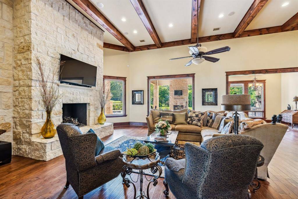 This inviting open-concept kitchen and family area features elegant wood beams, a stone accent wall, and large windows offering abundant natural light. The kitchen boasts a spacious island with granite countertops and rich wood cabinetry.