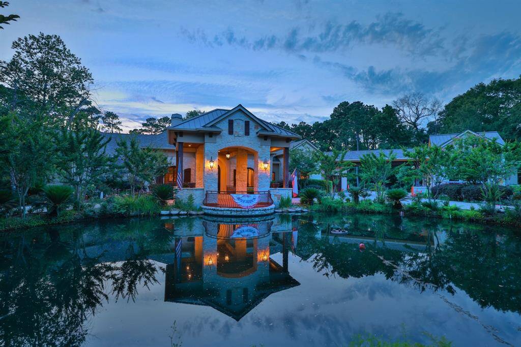 This stunning property features a gorgeous spacious one story house with a covered porch, beautifully reflected in a tranquil pond. Surrounded by lush greenery and mature trees, it offers a serene and picturesque setting perfect for relaxation.
