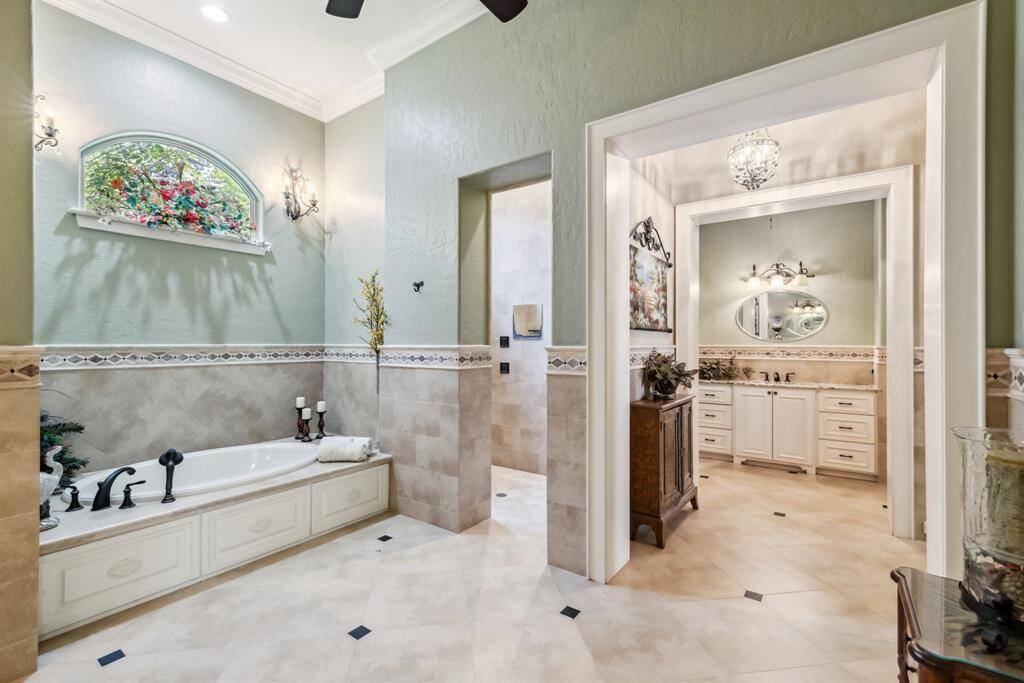 This secondary bedroom features an ensuite bathroom, elegant crown molding, rich wood floors, and charming shutters.