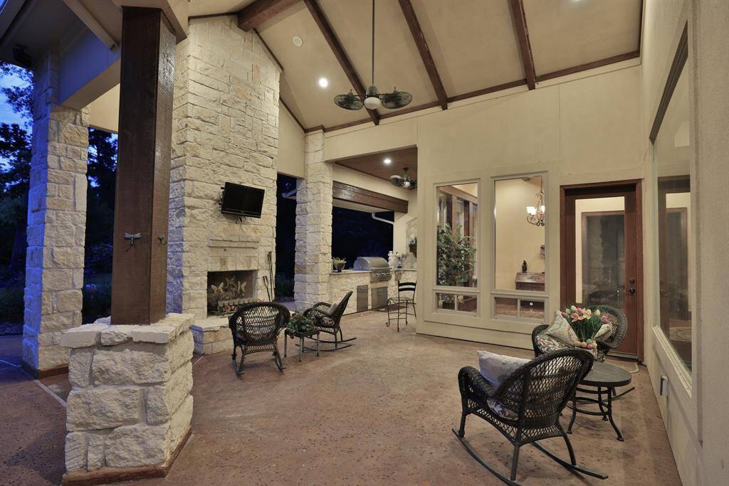 This sunset photo showcases a beautiful backyard with a modern pool surrounded by a spacious patio. The home features elegant stonework and outdoor seating, perfect for entertaining, all set against a tranquil wooded backdrop.
