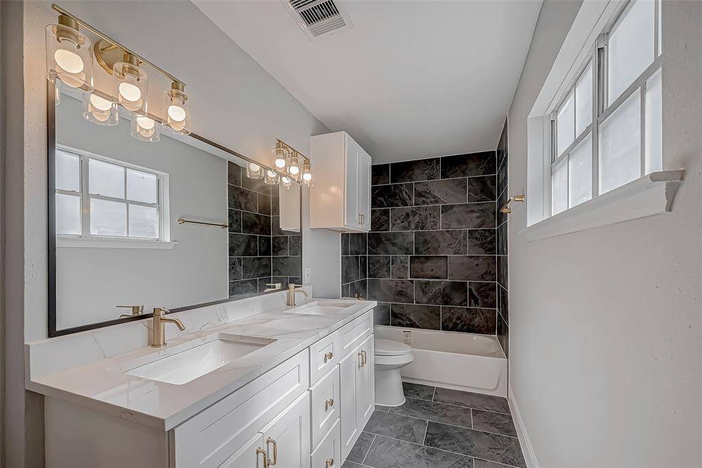 Beautiful upstairs bathroom with double vanities, black tile tub surround, white shaker cabinets and modern gold accents.