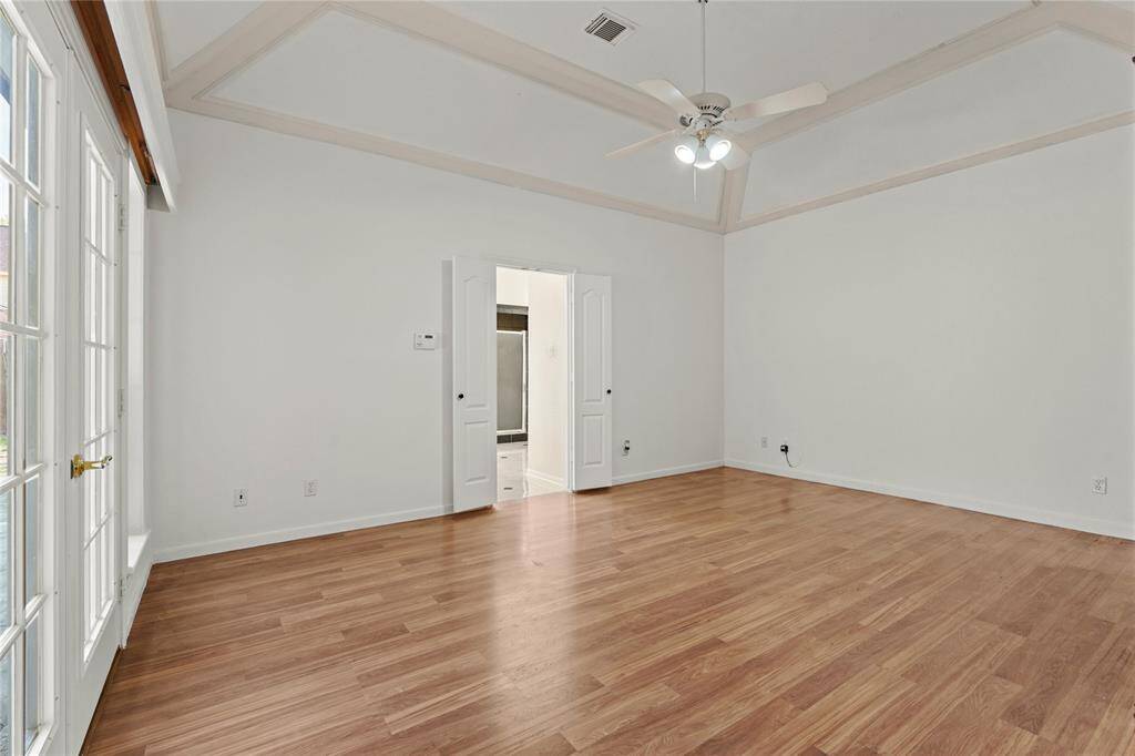 This spacious priary room offers endless possibilities! The soaring tray ceiling adds architectural elegance, while the warm wood flooring brings a cozy touch. Built-in bookshelves provide the perfect space for a personal library, decorative displays, or additional storage. A wall of French doors and windows fills the room with natural light and offers seamless access to the outdoor patio, making it an ideal space for relaxation or creativity.