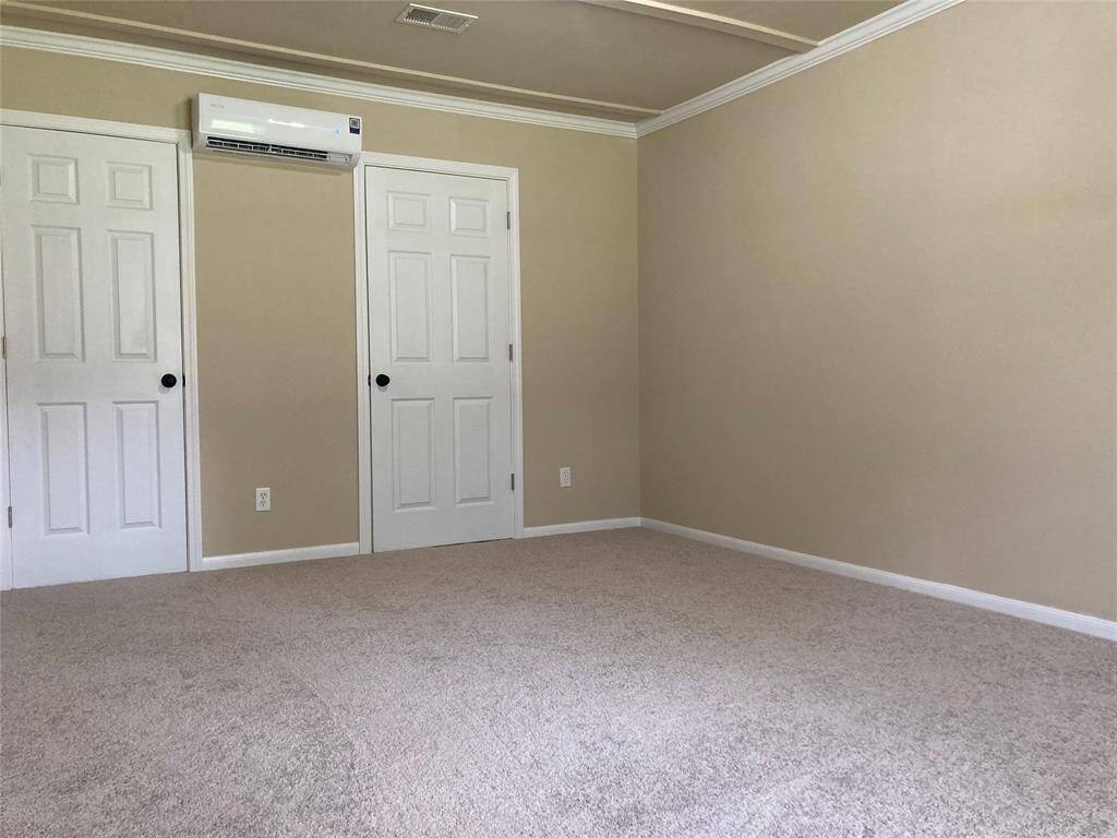 Bedroom 4 features neutral walls with crown molding, and carpeted flooring. It’s equipped with a wall-mounted air conditioning unit, providing a comfortable and versatile space.