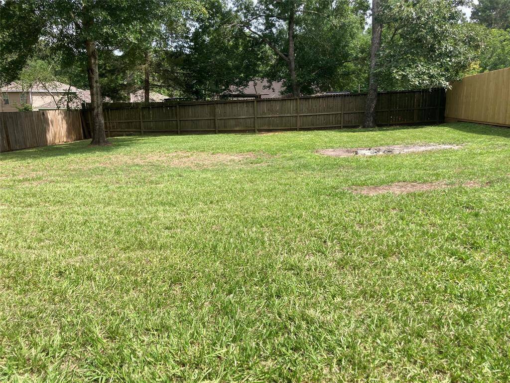 Spacious backyard with lush green grass, mature trees, and a wooden privacy fence, offering a serene and private outdoor space.