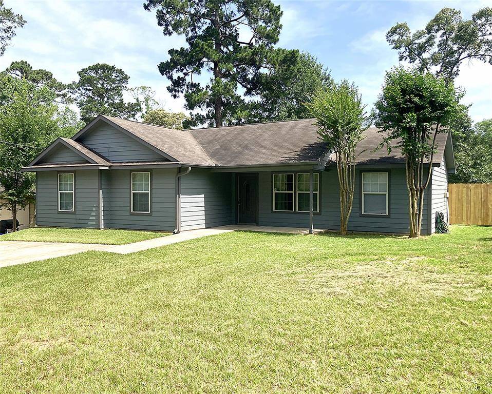 Charming single-story home with a modern gray exterior, surrounded by mature trees. It features a well-maintained lawn and a welcoming front porch. Perfect for those seeking a cozy, inviting space.
