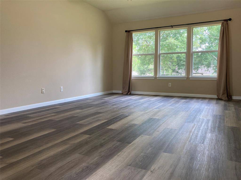 This spacious room features large windows allowing natural light to flood in, complemented by elegant wood-look flooring and neutral walls, creating a bright and inviting atmosphere.