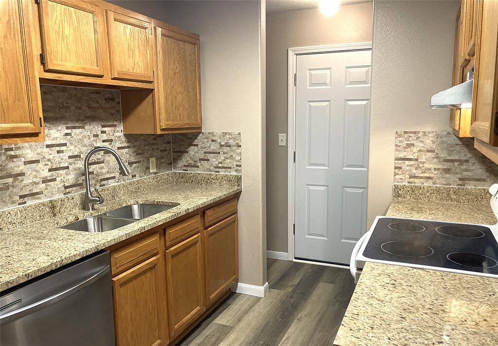 This kitchen features granite countertops, a double sink, and a backsplash. It has wooden cabinets, a smooth-top stove, and LVP flooring, providing a functional and stylish cooking space.