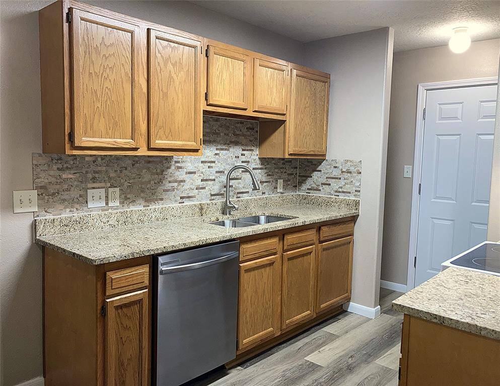 This kitchen features wooden cabinetry, granite countertops, and a modern backsplash. It includes a stainless steel dishwasher and a double sink.