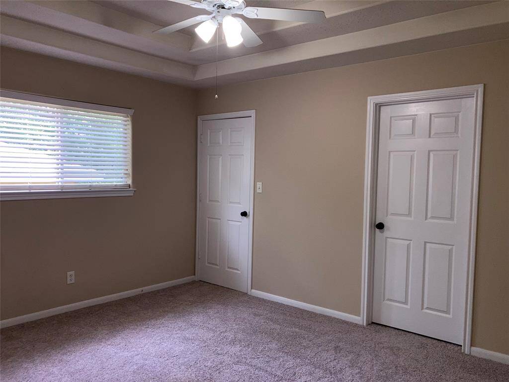 Primary room features beige walls, carpet flooring, a ceiling fan, and on suite bathroom. A window allows natural light in, creating a cozy atmosphere.