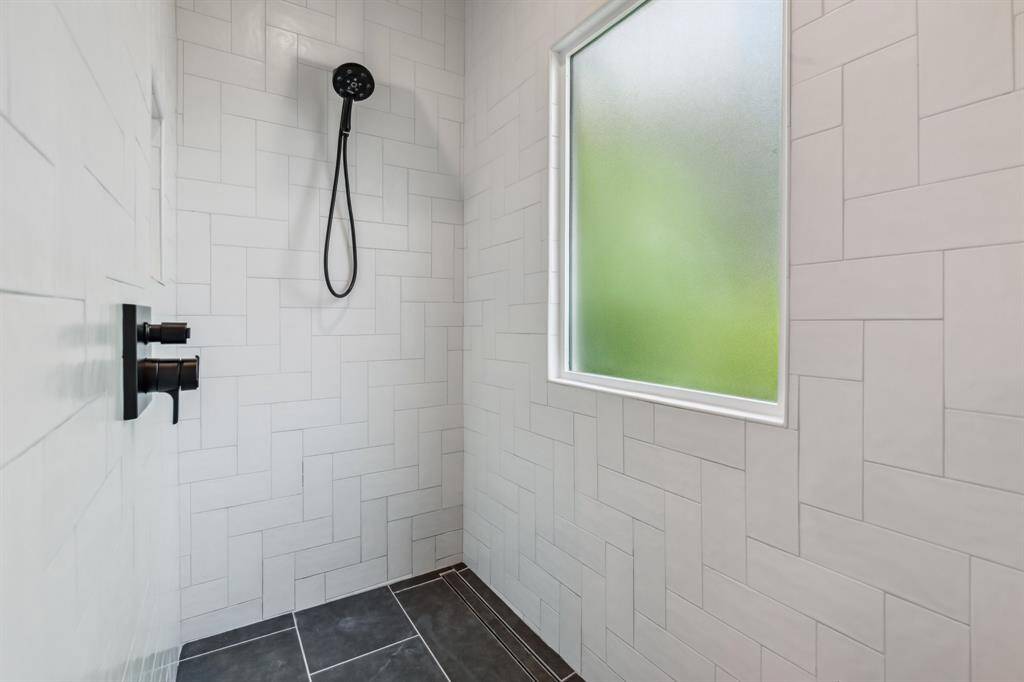 Inside the beautifully updated walk-in shower, you’ll find a window, shampoo niche, herringbone tile and matte black fixtures.