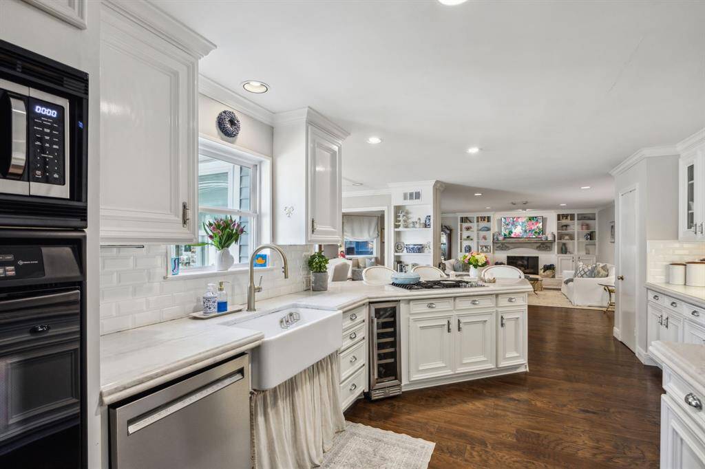 Another view of the kitchen showing the farmhouse sink and stainless steel dishwasher.