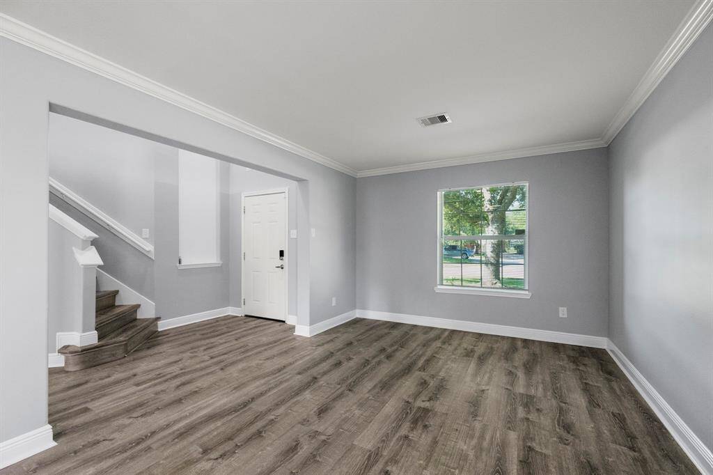 Welcoming front room with rich flooring, crown molding, and natural light—perfect for a sitting area or home office.