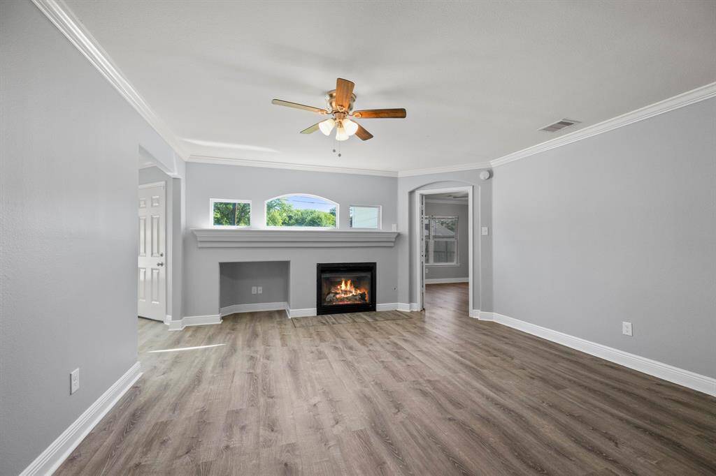 Spacious living room with cozy fireplace, ceiling fan, crown molding, and natural light—ideal for relaxing or entertaining.