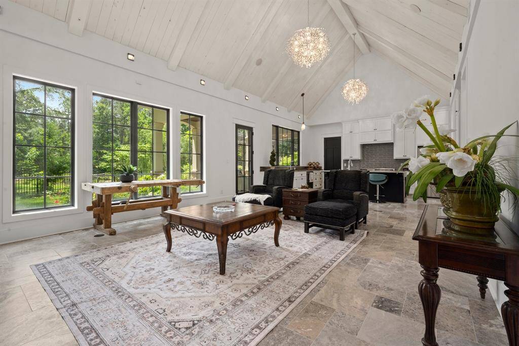 The vaulted ceiling, finished with white-painted wood paneling and exposed beams, creates an expansive and airy feel, emphasizing vertical space.  Statement chandeliers hang at varying heights, catching the light in intricate patterns and adding a touch of contemporary chic that complements the clean rustic design of the interior.