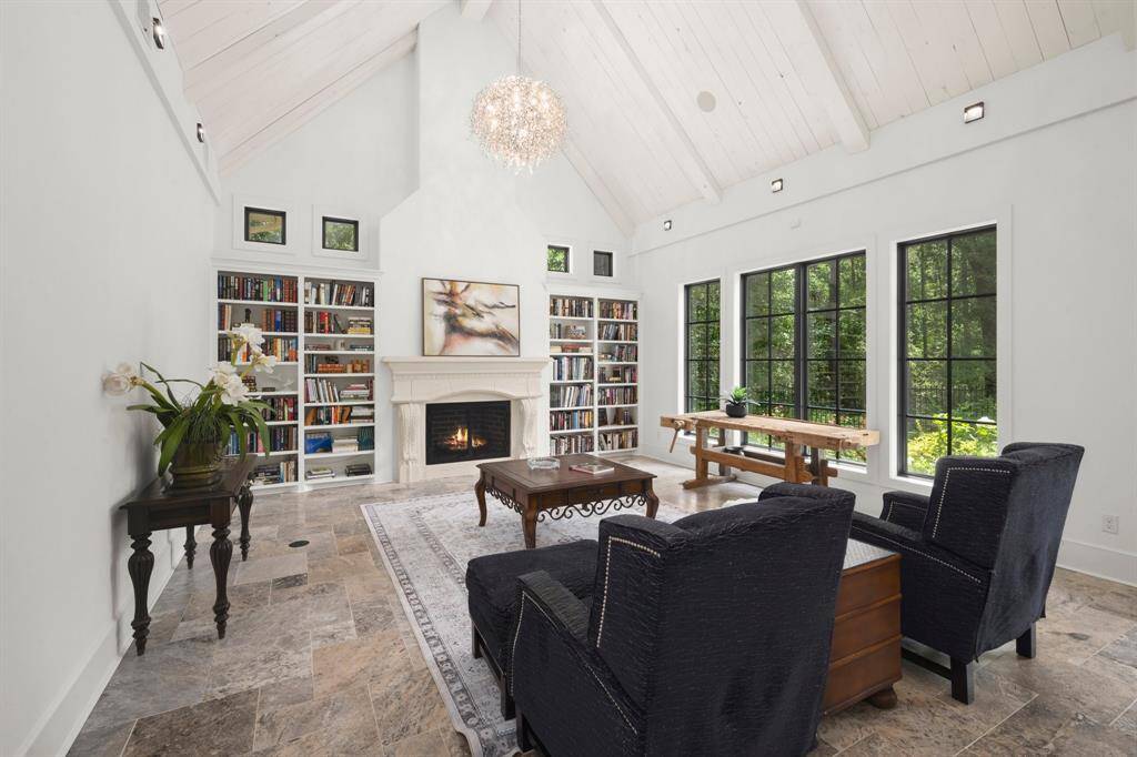 The abundant natural light shines through tall, custom-designed black-framed windows that offer a stunning view of lush greenery outside, making the interior feel open and connected to nature.