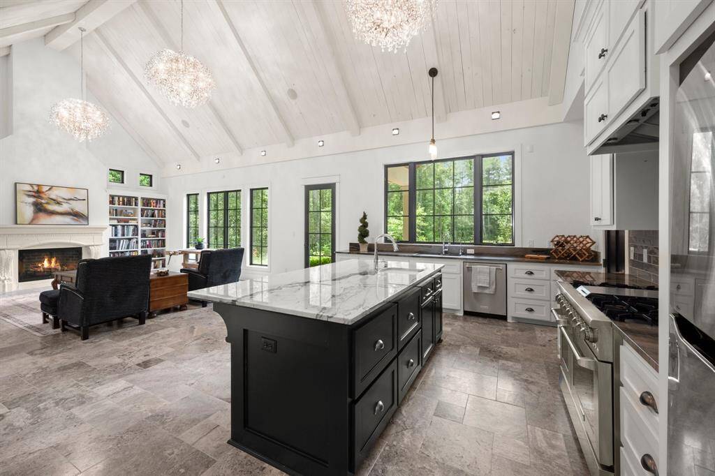 The kitchen features white cabinetry, bold black accents on the backsplash, and a stainless steel professional-grade 6-burner double oven range, matching the home’s central themes of contrast and flow.