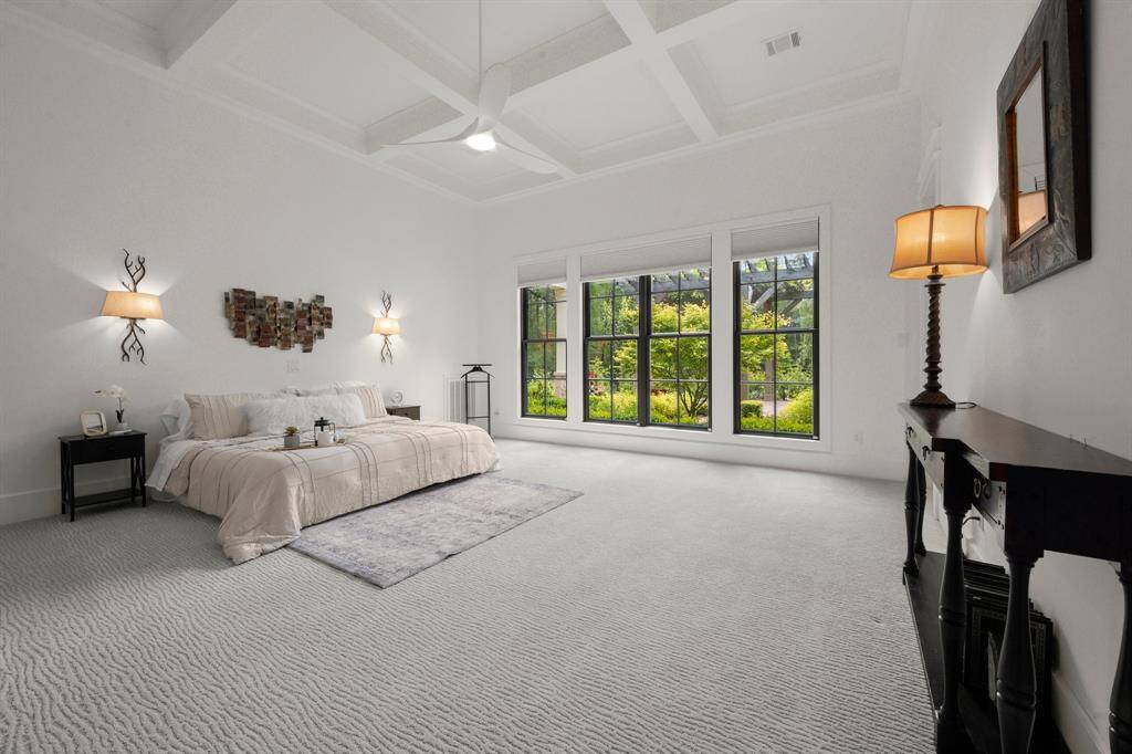 The coffered ceiling detail and built-in sconce lighting enhance the downstairs primary bedroom's neutral palette.