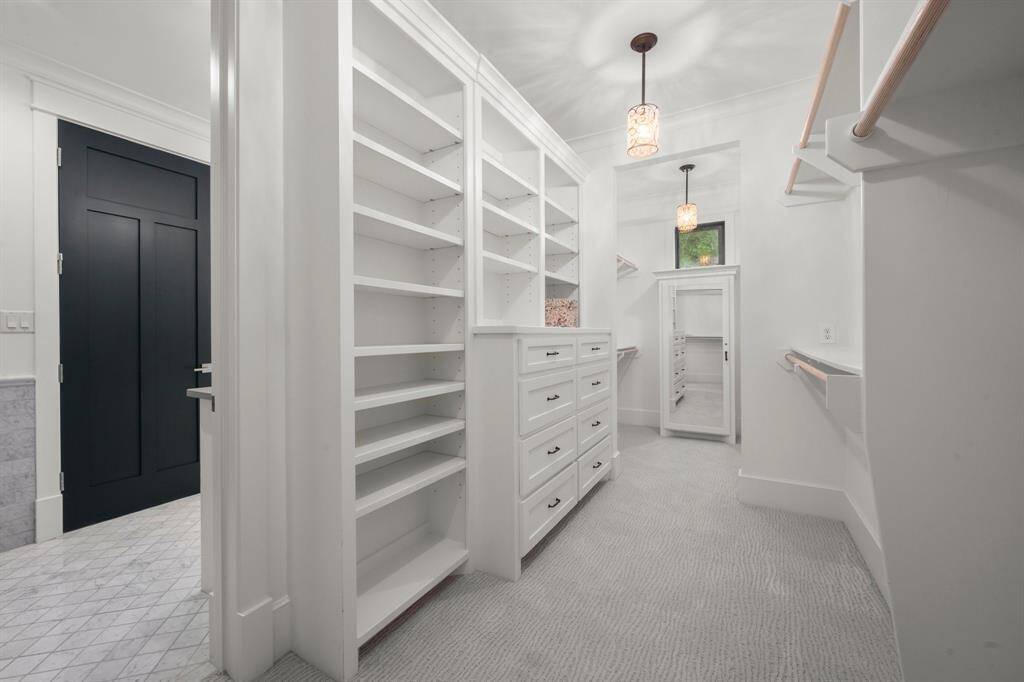 The most expansive of the two primary bedroom closets, with elegant pendant lighting, a variety of wall-to-wall custom-built-in storage solutions - soft-close drawer storage, a sizeable, lockable jewelry storage cabinet, various heights of shelving, and hanging storage ideal for organized storage.