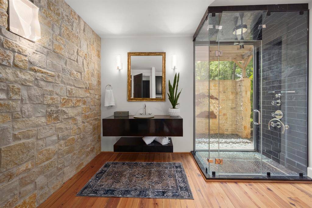 One of the two en suite primary bathrooms is uniquely defined with a stacked stone wall, reclaimed antique pine wood floors, a modern floating vanity, luxury spa-quality shower that brings nature, once again, inside of the home while still offering privacy via a matching stacked stone wall.