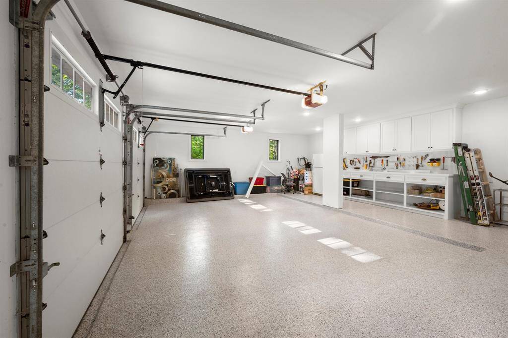 Oversized two-car garage. 9' insulated quiet close garage doors, epoxy flooring, built-in upper cabinets, lower shelving, and pegboard wall for storage and organization.