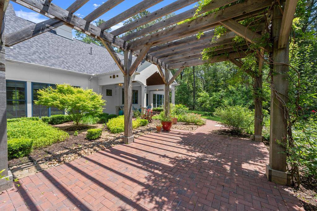 Expanded outdoor living on the cobblestone-lined lined complete with a wooden pergola adorned with maturing wisteria. The well-maintained garden features lush greenery and potted plants, providing a serene and inviting atmosphere.