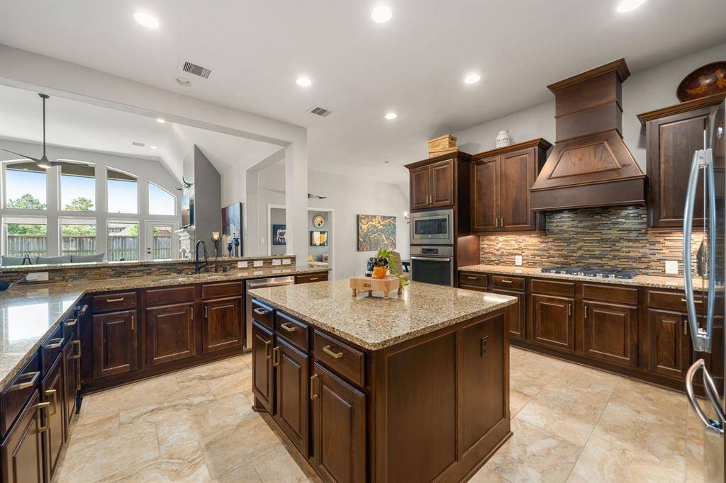 This stunning kitchen displays such a beautiful contrast with the dark stained cabinets, neutral paint, granite countertops, tile backsplash, SS appliances, kitchen island with extra storage, breakfast bar, recessed lighting, high ceilings and walk in pantry.