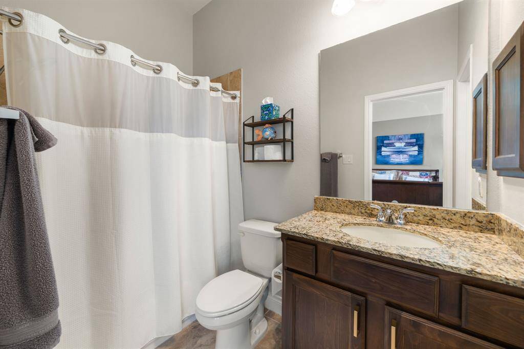 Secondary bedroom features wood like tile flooring, neutral paint, dark stained ceiling fan with lighting and a large window with privacy blinds.