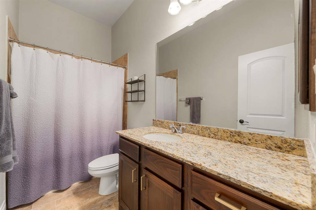 Secondary bedroom features wood like tile flooring, neutral paint, dark stained ceiling fan with lighting and a large window with privacy blinds.