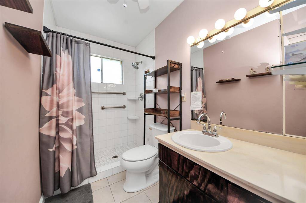 This bathroom features a spacious walk-in shower with hexagon tile flooring in the shower and tiled walls. It includes a vanity with a large mirror, and under sink cabinets for added storage and convenience