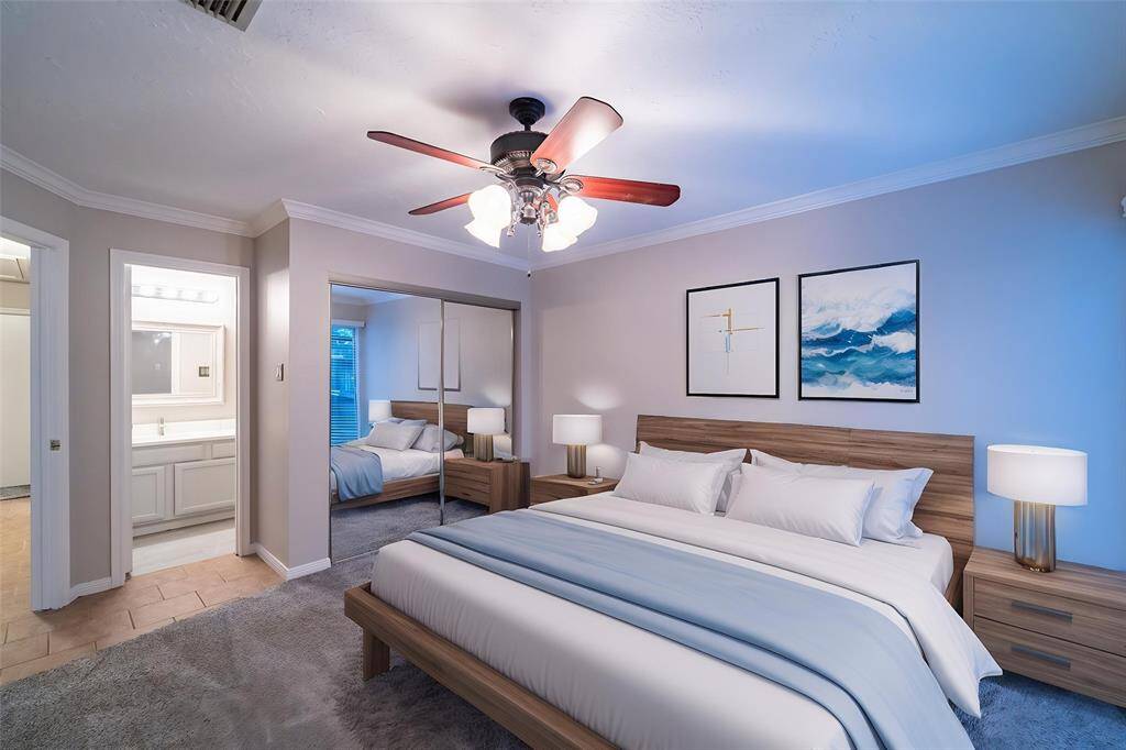 This inviting bedroom features a comfortable bed with a wooden frame, modern decor, and ample natural light. A ceiling fan adds comfort, while mirrored closet doors enhance space. An en suite bathroom offers convenience.