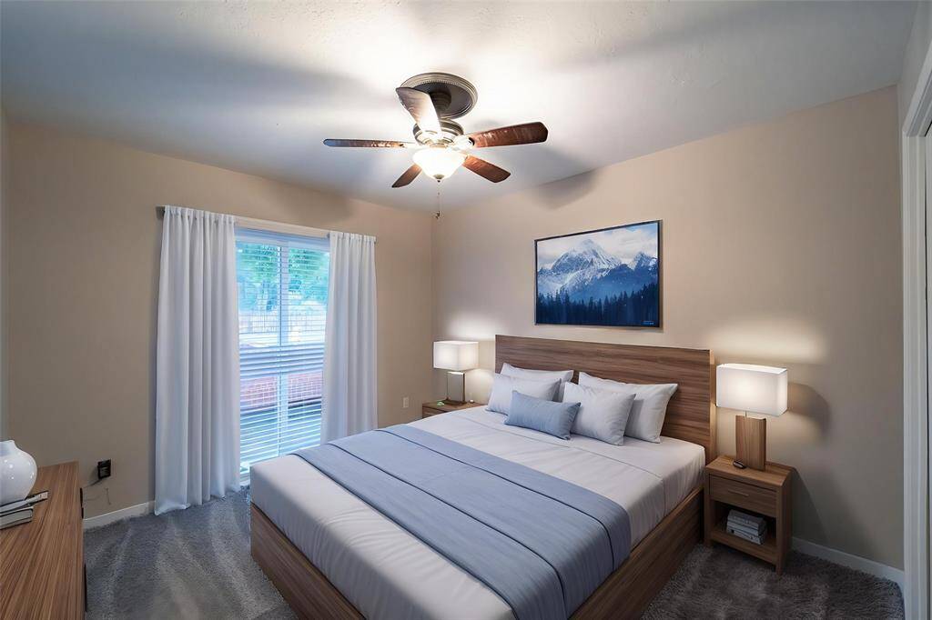 This cozy bedroom features a neutral color palette with a large window providing natural light. It includes a ceiling fan, and modern finished floors and walls.