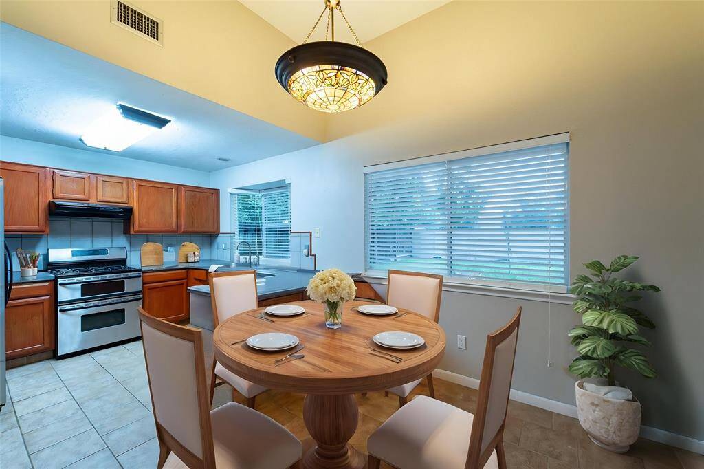 This inviting kitchen features wooden cabinetry, stainless steel appliances, and tiled flooring. Adjacent is a cozy dining area with a dining area, illuminated by a stylish overhead light. A large window provides natural light and a view of the outdoors. This room has access to the sizeable, fully fenced in, backyard.