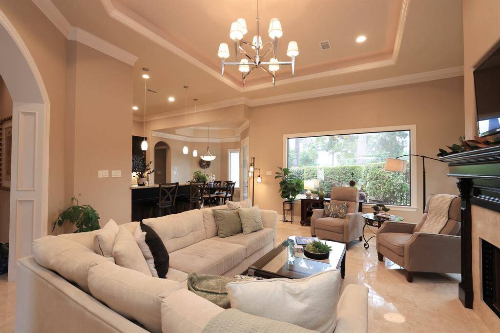 This spacious living area features an open floor plan with elegant tray ceilings and recessed lighting. Large windows provide plenty of natural light, while the neutral tones and cozy seating create a warm, inviting atmosphere. The room seamlessly connects to a dining area and kitchen, ideal for entertaining.
