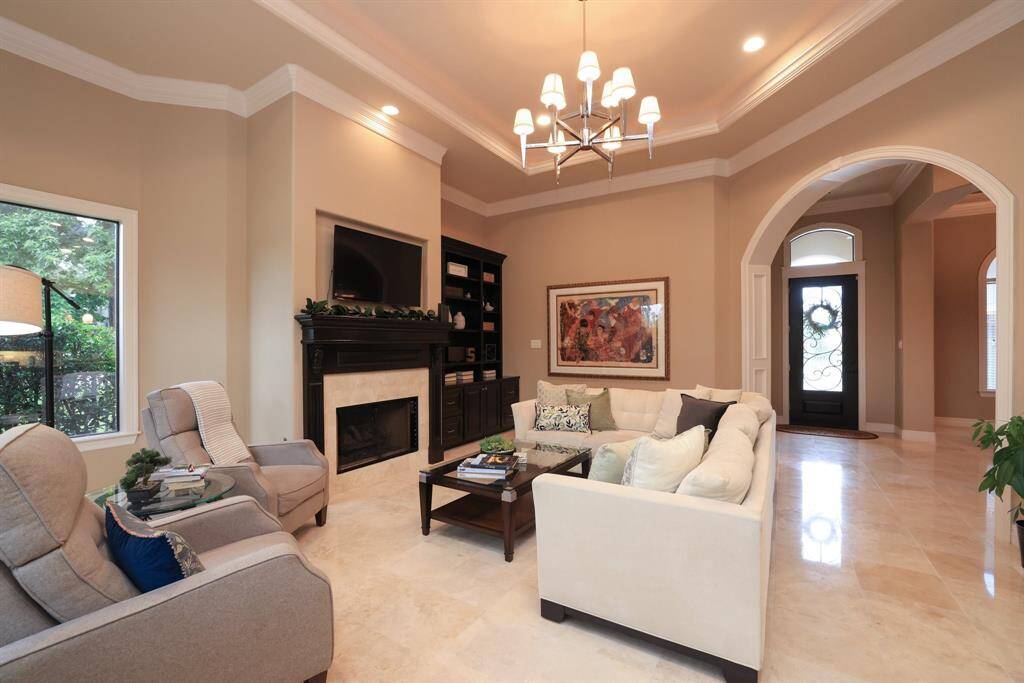 This inviting living area features a stylish tray ceiling with a modern chandelier and a custom built-in for ample storage and display.