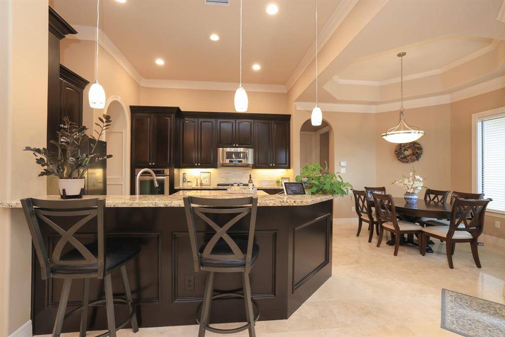 This photo showcases a stylish kitchen and dining area with dark wood cabinetry, granite countertops, and pendant lighting. The open layout also features a breakfast bar with comfortable seating.