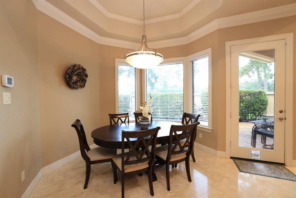This breakfast room accommodates a large, cozy round table, ideal for hosting guests. It features a stylish chandelier, expansive windows with backyard views, and a glass door leading to an inviting patio.