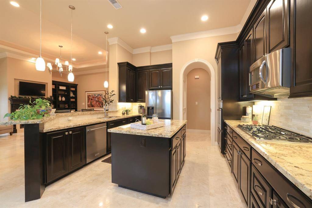 This spacious kitchen features elegant dark wood cabinetry, granite countertops, and modern stainless steel appliances. It boasts an open layout with a central island with cabinetry.